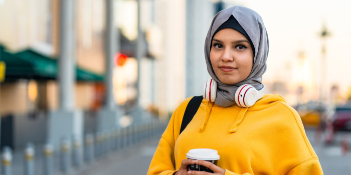 Woman wearing a head covering smiling and holding a coffee